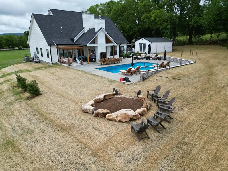 Aerial view of a white custom home by Outback Construction with pool, covered porches and a stone fire pit ring