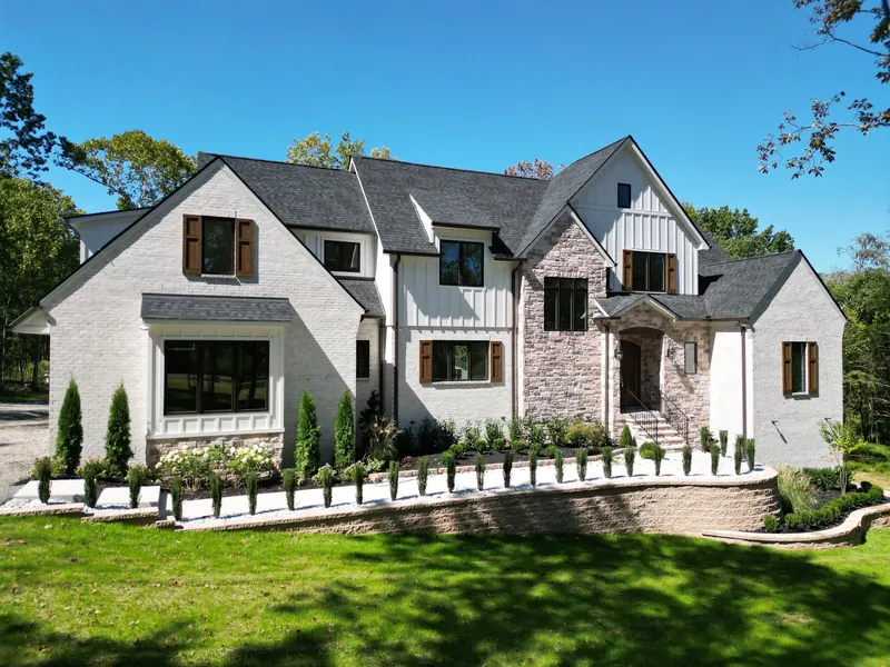 Two-storey custom home built by Outback Construction: white brick and stone facade, steep gables, dark windows, landscaped front elevation