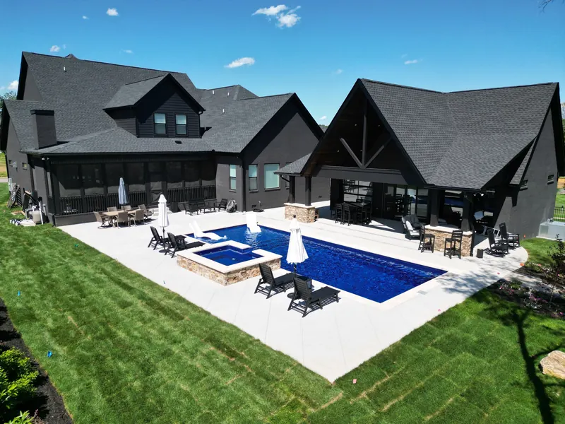 Aerial view of a dark-exterior custom home by Outback Construction with steeply pitched roofs, pool, spa and a full outdoor kitchen